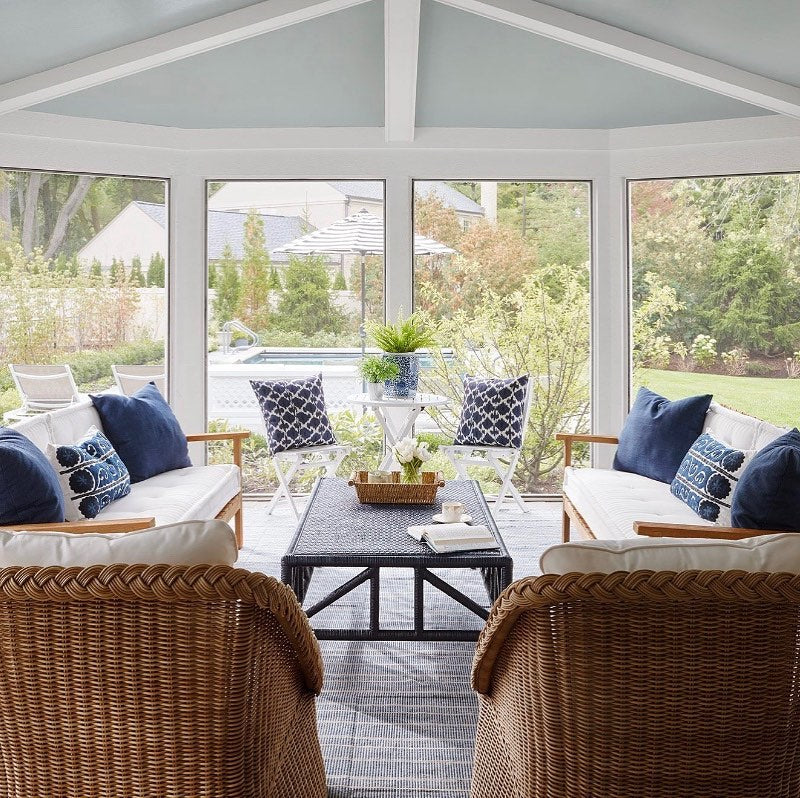 Bright, enclosed patio with wicker furniture, fresh flowers, and plants