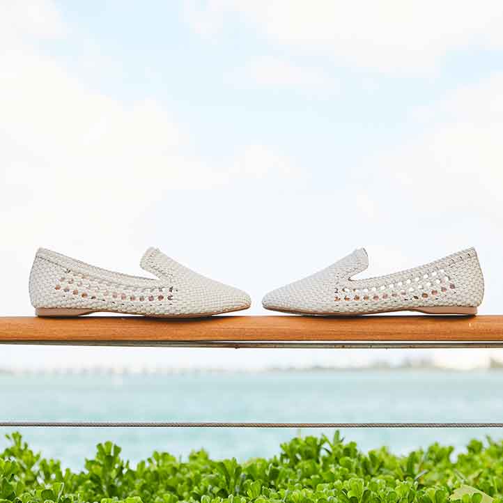 White handwoven, vegan leather flats against ocean background 