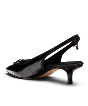 Black patent leather slingback kitten heel with pointed toe and delicate bow detail, featuring a glossy finish. Back angled view.
