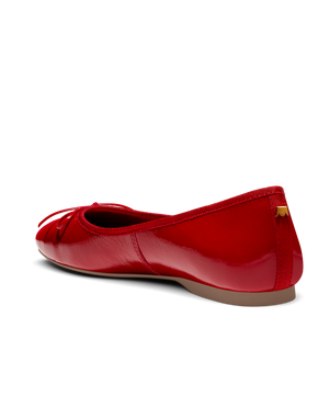 Red patent leather ballet flat with delicate bow detail, featuring a glossy finish. Back angled view.